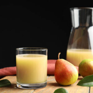 Fresh pear juice in glass and fruits on wooden table
