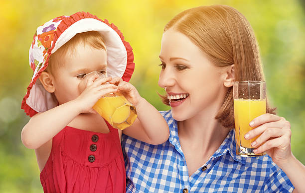 Family mother and baby daughter drinking orange juice in the summer outdoors